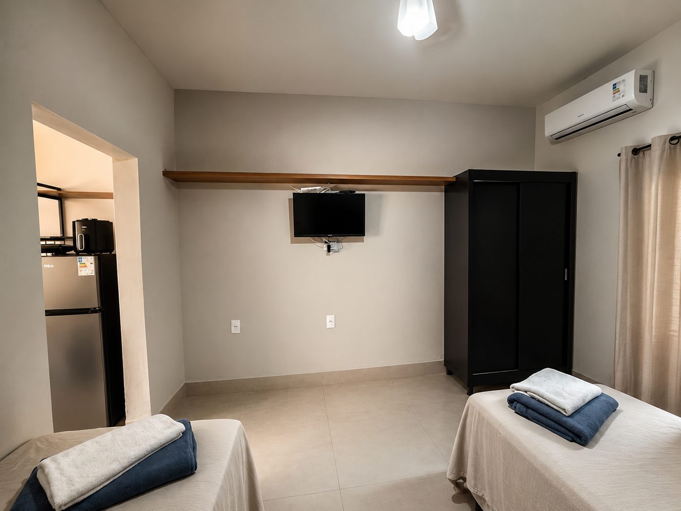 Quarto com televisão, guarda-roupa e acesso à cozinha